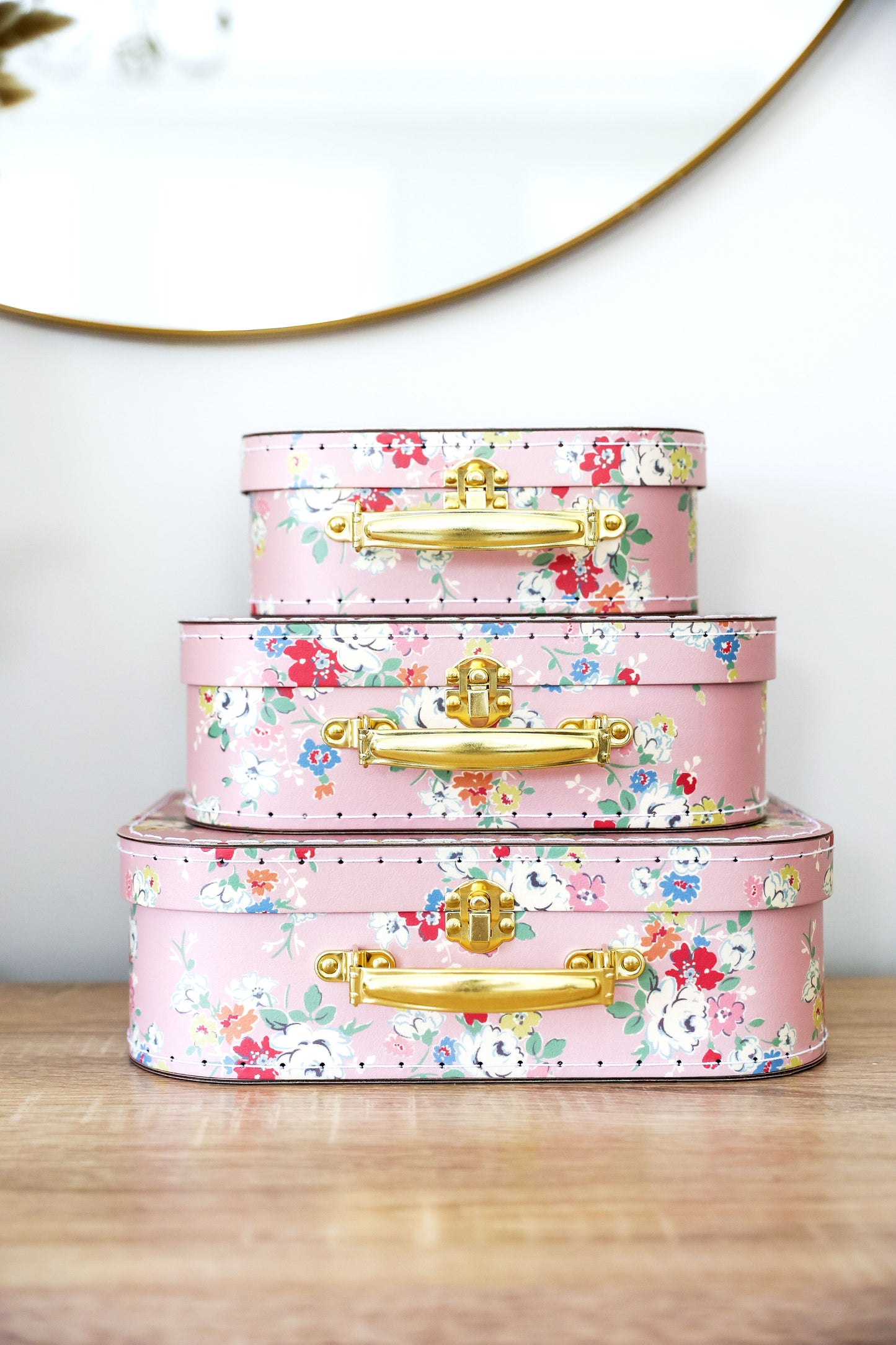 Charming vintage rose kids carry case set in three nesting sizes with gold handles on a wooden table.