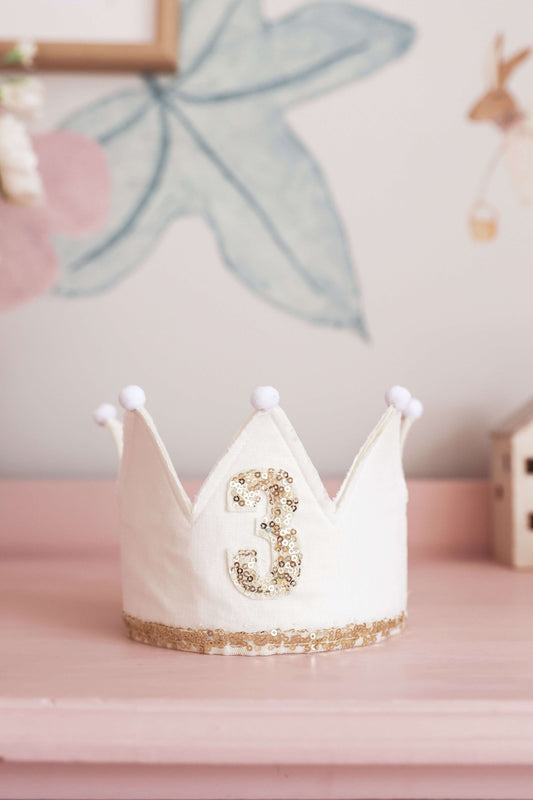 Adjustable ivory crown with gold sequins for a 3rd birthday celebration, featuring ribbon ties and felt accents.