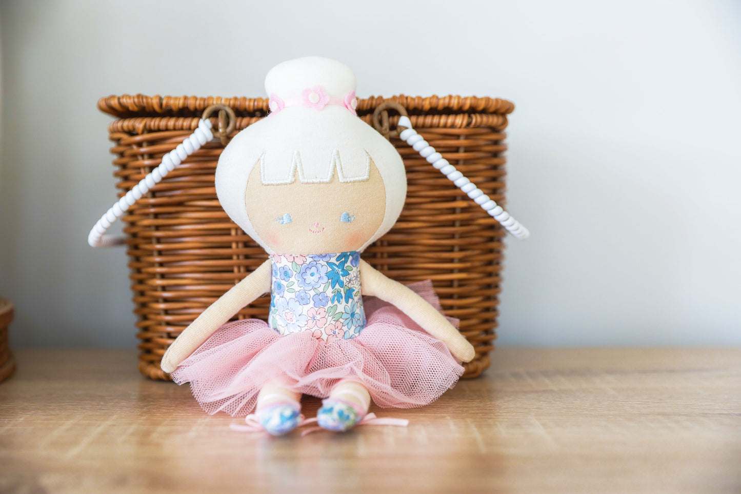 Baby ballerina doll in a fluffy tulle tutu and floral bodice, seated with a wicker basket in the background.
