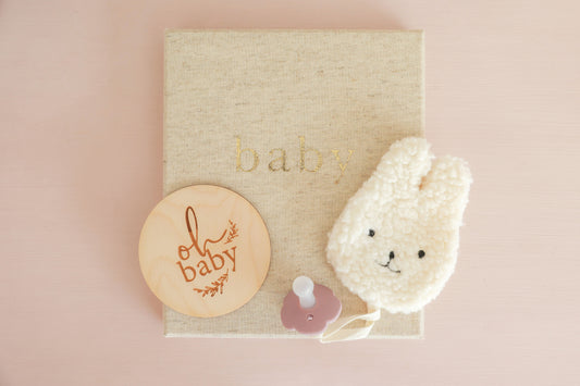Sherpa Paci Comforter Bunny Ivory with pacifier and wooden baby plaque on a soft background, perfect for soothing infants.