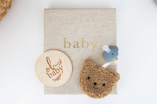 Sherpa bear pacifier comforter in caramel color, attached to a calming pacifier, displayed on a baby-themed background.