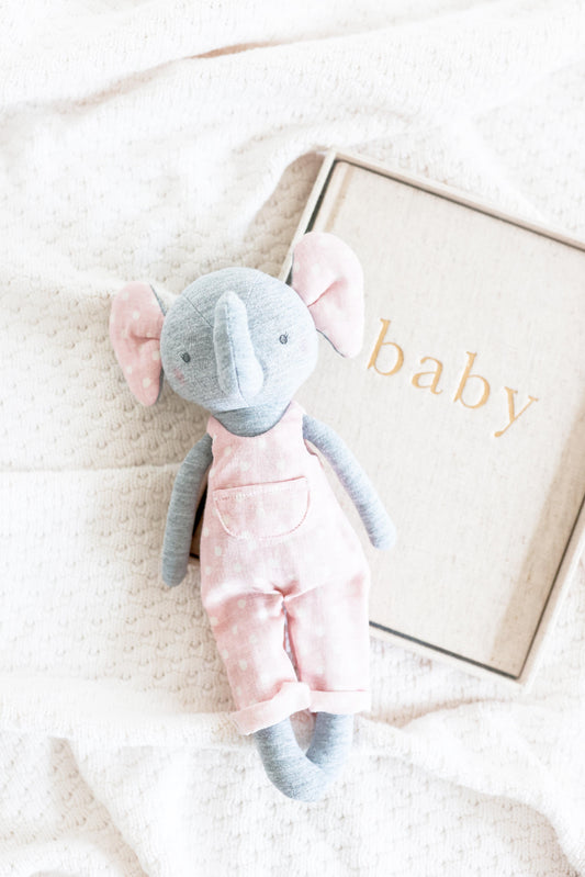 Edith Elephant plush toy in pink cotton overalls, 28cm tall, next to a book titled 'baby'. Handcrafted and adorable.