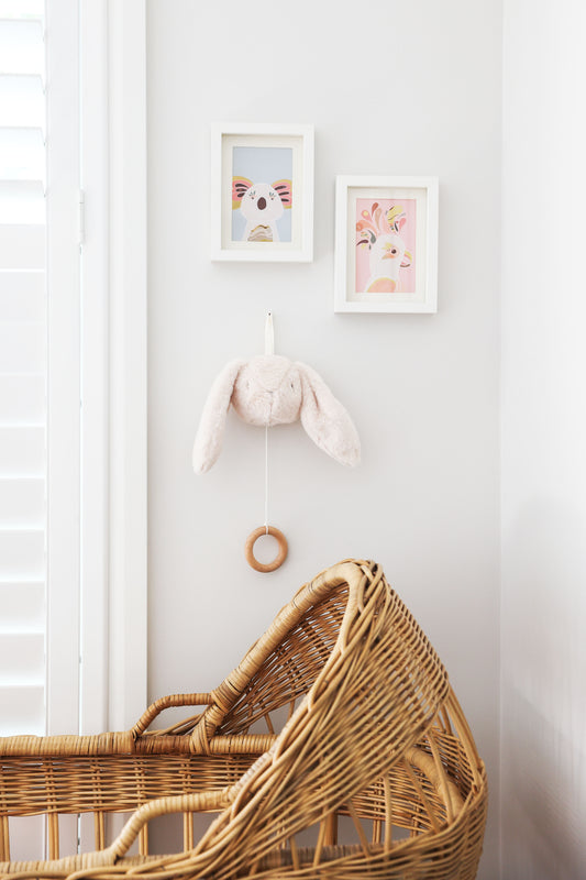 Alimrose Darcey Bunny Musical hanging near a wicker bassinet and framed bunny art in a nursery setting.