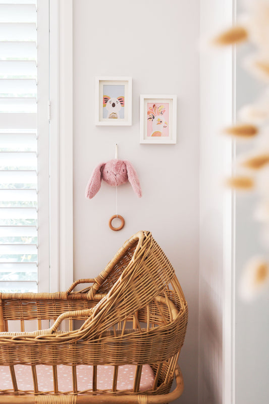 Cozy nursery featuring a wicker bassinet and pink Darcey Bunny Musical hanging on the wall.