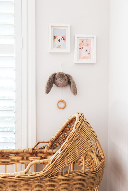 Alimrose Darcey Bunny Musical hanging near a stylish wicker bassinet in a bright nursery.