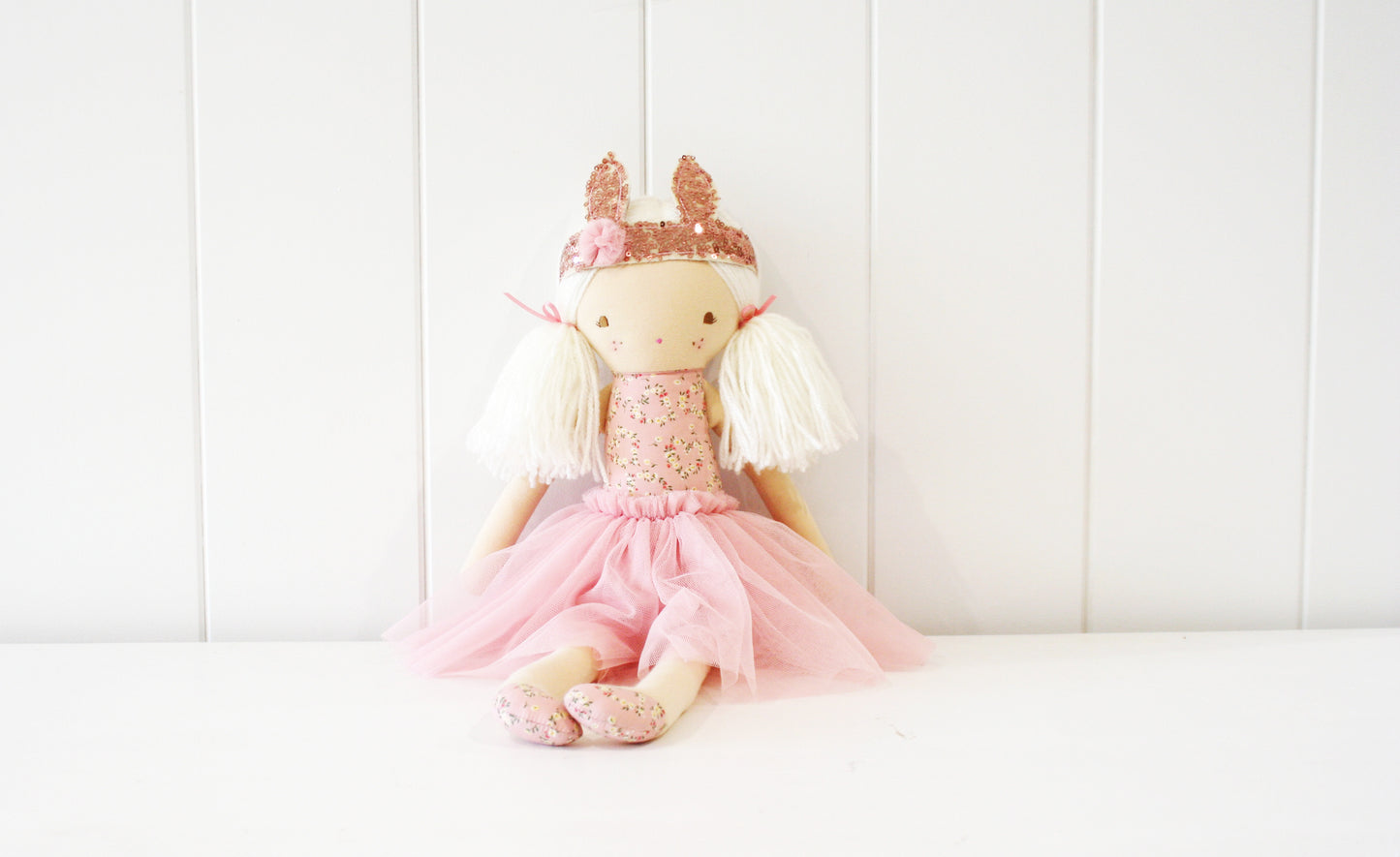 Soft fabric doll with cream-colored body, white yarn hair, pink dress with tulle skirt, and heart-patterned crown.