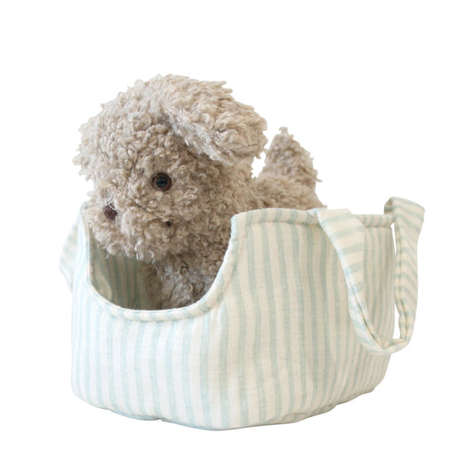 Soft beige plush puppy with curly fur sitting inside a light blue and white striped fabric carrier bag.