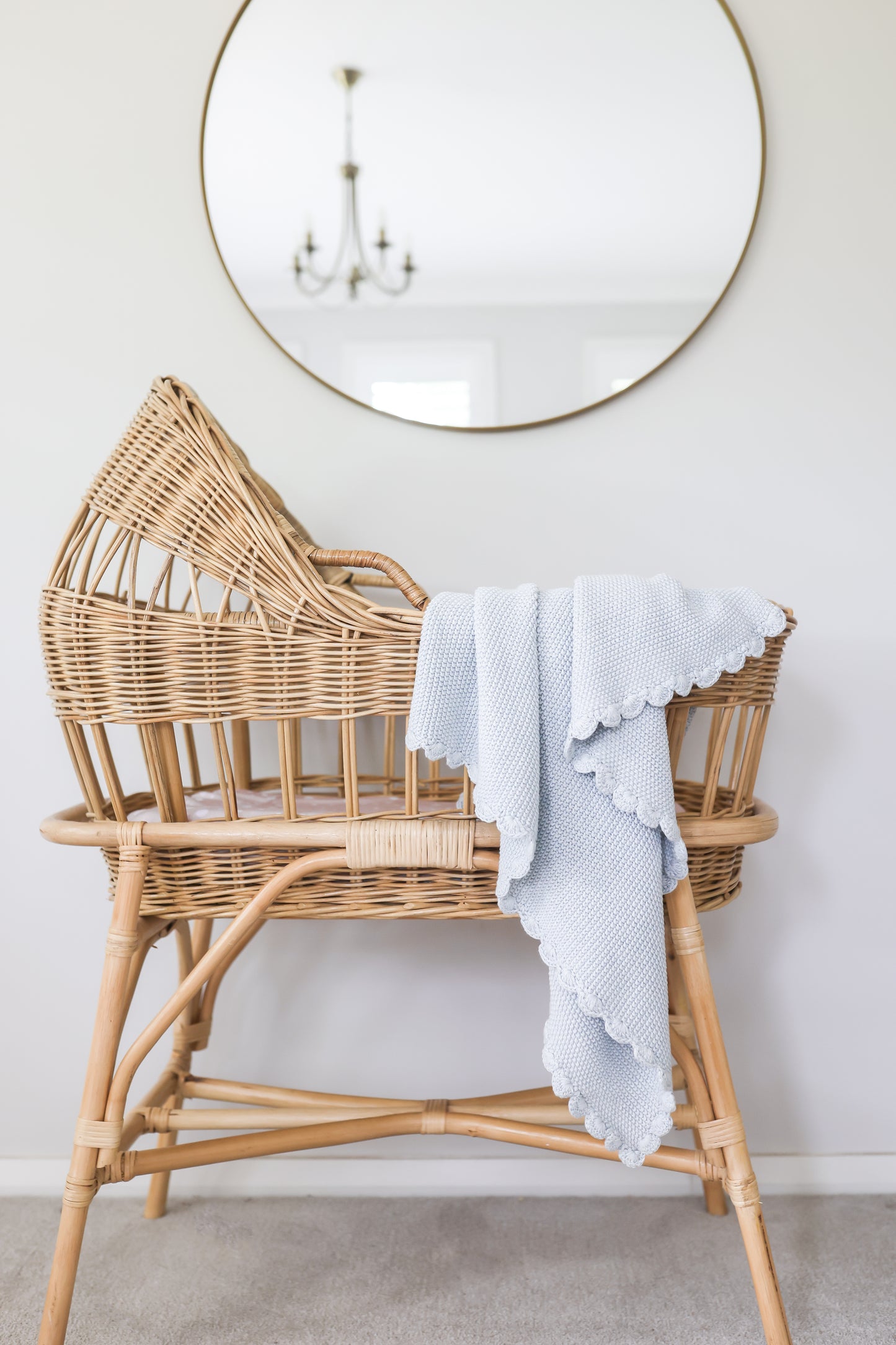 Powder blue knit baby blanket with moss stitch draped over natural rattan cradle with scalloped edges.