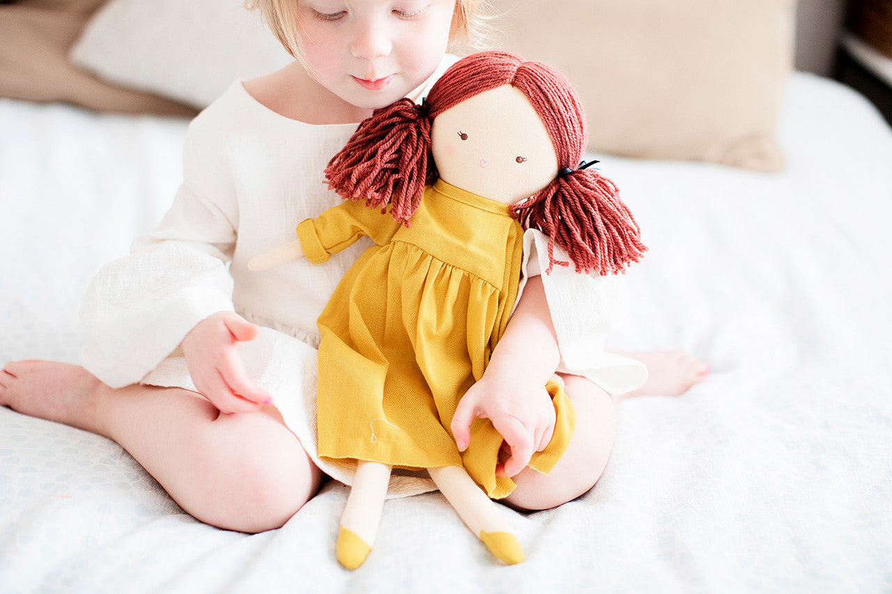 Child sitting with Matilda 45cm doll in a butterscotch dress and piggy tails, perfect for imaginative play.
