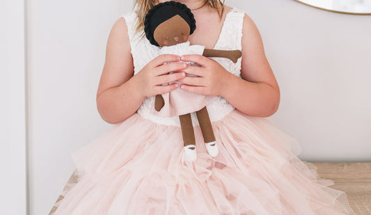 Child holding Baby Coco doll in pale pink dress, showcasing cotton material and embroidered features.