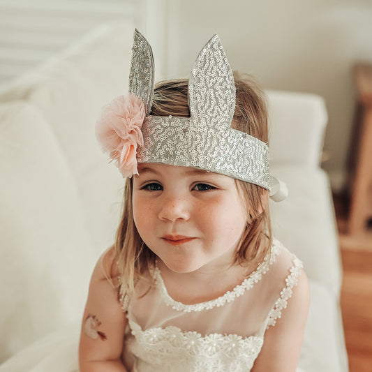 Child wearing a sparkly silver sequin bunny crown with a ribbon tie and flower decoration.