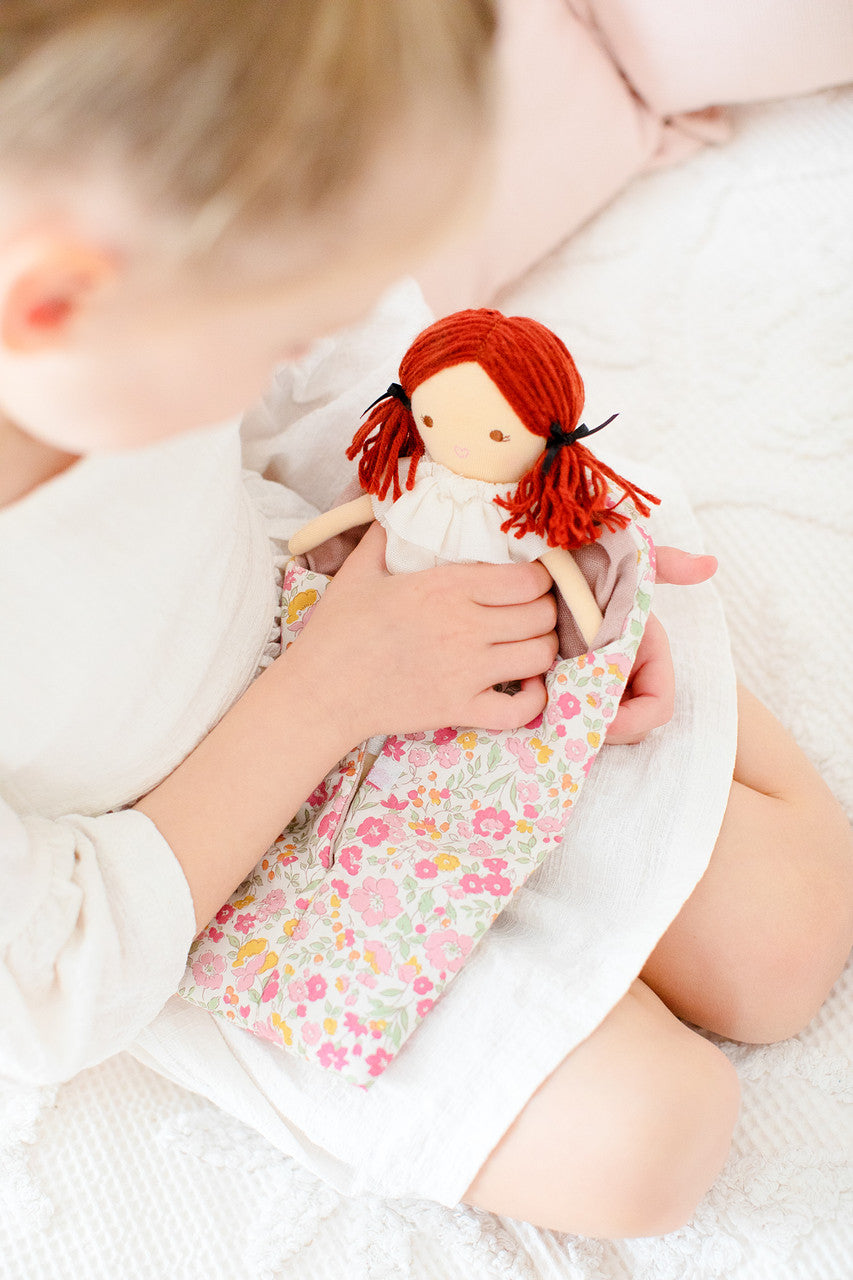 Child holding Mini Matilda asleep/awake doll in a floral sleeping bag, promoting developmental play and imagination.