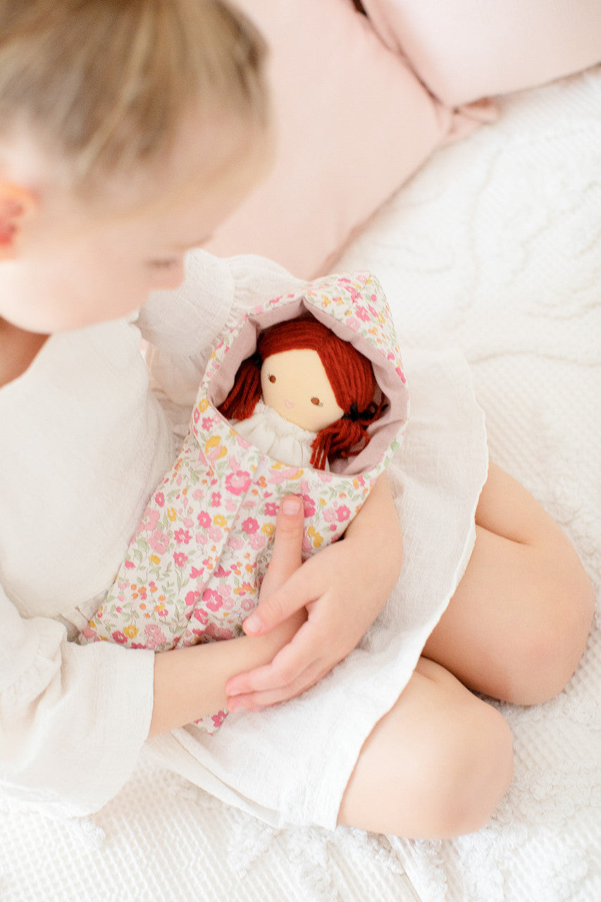A child cuddles the Mini Matilda doll in a floral mini sleeping bag, highlighting playful developmental fun.