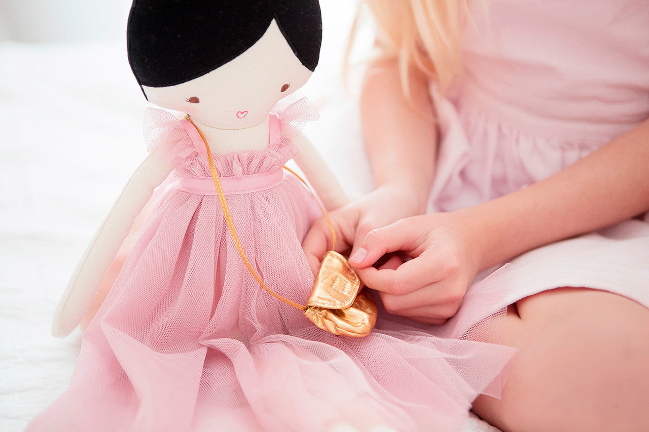 A child playing with an Alimrose Charlotte Doll dressed in a pink tulle gown, holding a mini golden bag.