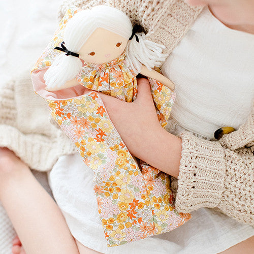 Child holding Mini Matilda Asleep Awake doll in floral dress, cuddled in a cozy blanket. Perfect for ages 3 and up.