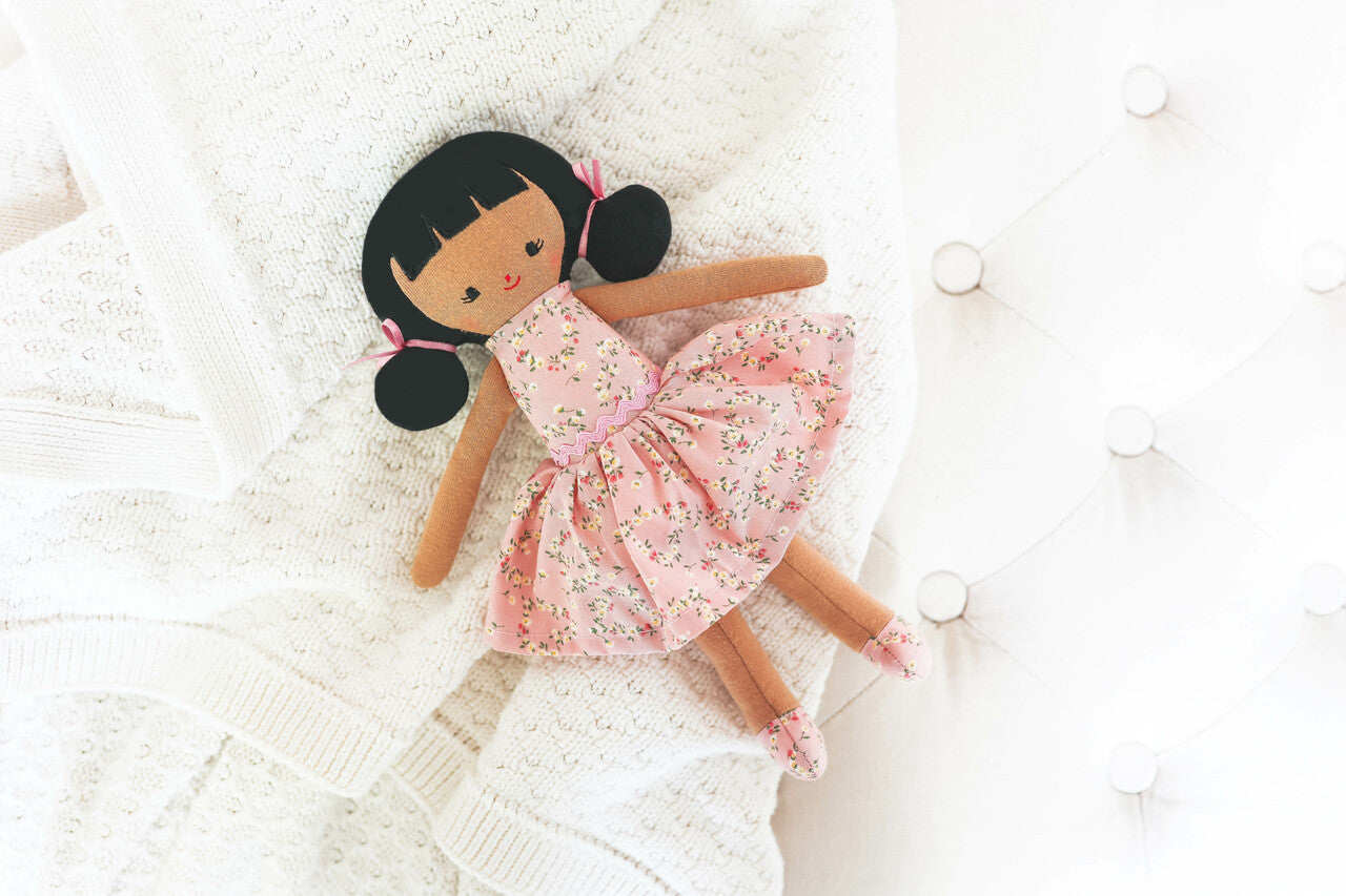 Alimrose Audrey Doll 26cm with floral dress and side buns, perfect companion for kids, resting on a cozy blanket.