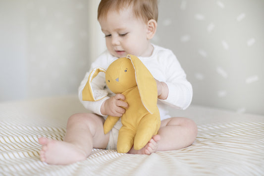 Baby cuddling a soft butterscotch linen bunny toy; perfect snuggle buddy for little ones.