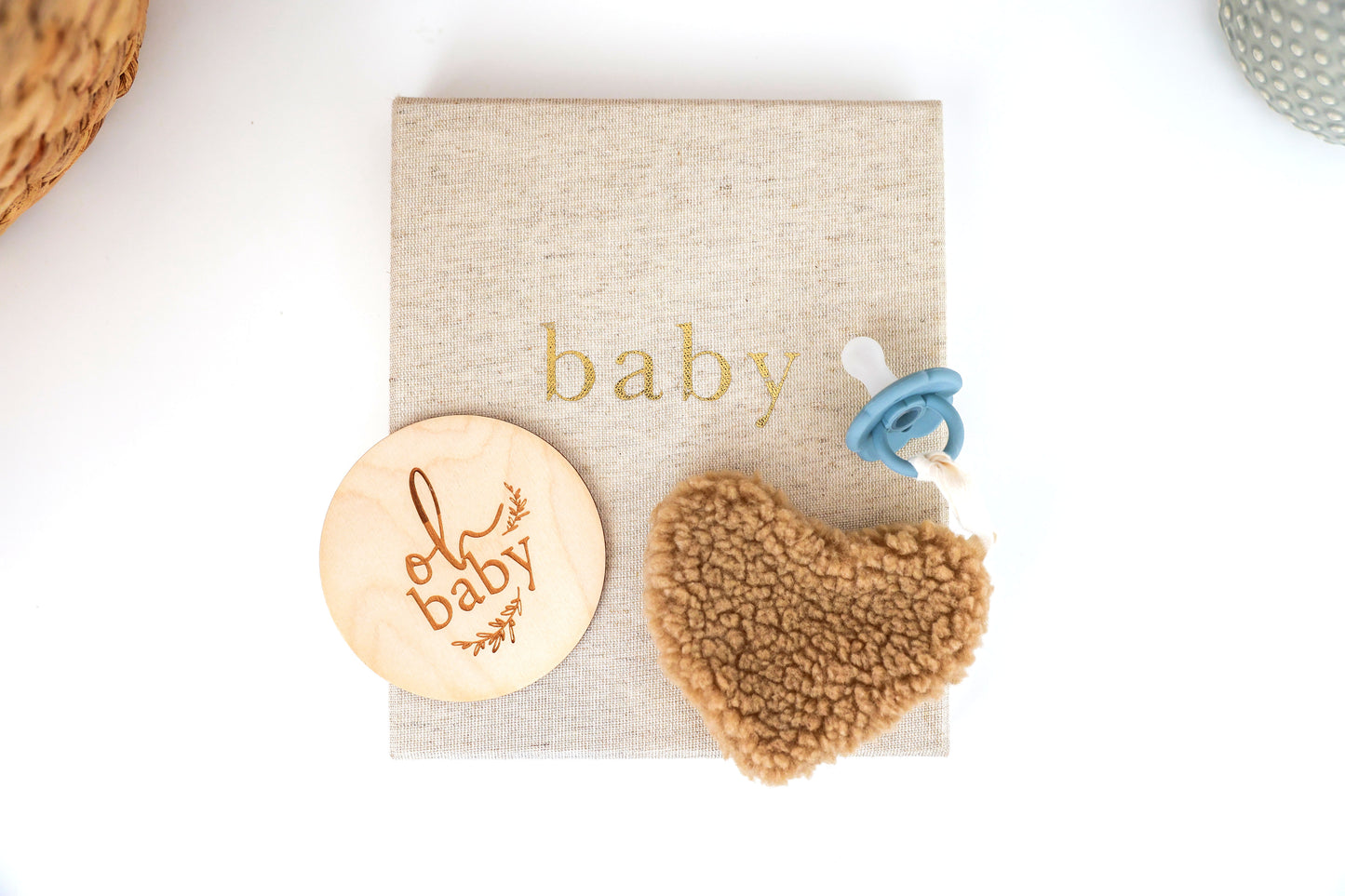Caramel-colored heart-shaped sherpa comforter with attached blue pacifier on beige baby-themed fabric background.