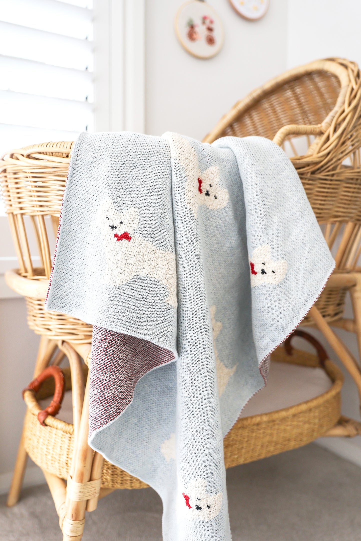 Soft light gray baby blanket with white Westie puppy faces and red bow details draped over wicker chair.