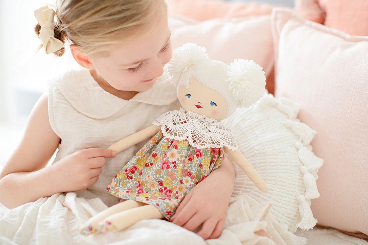 Cloth doll with white yarn hair styled in buns, floral dress, and crocheted collar held by smiling girl in white dress.