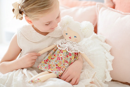 Cloth doll with white yarn hair styled in buns, floral dress, and crocheted collar held by smiling girl in white dress.