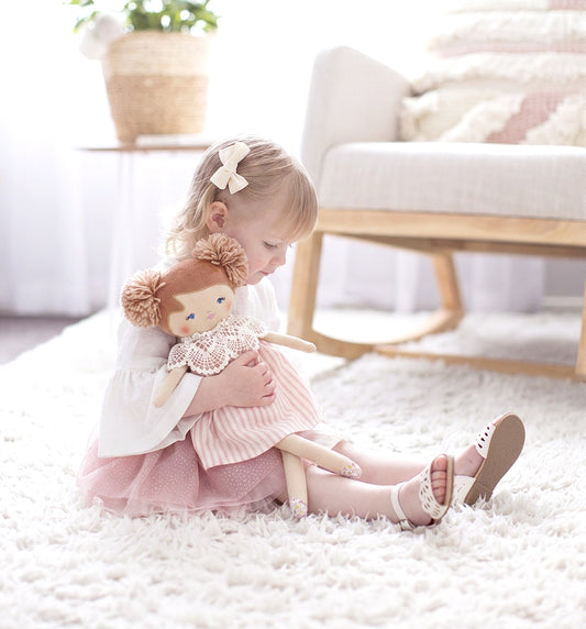 45cm fabric doll with pink striped dress, brown yarn hair, and lace collar, held by a child sitting on a white rug.