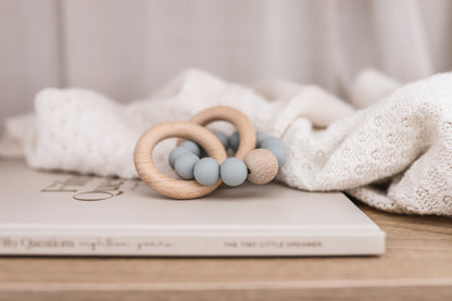 Beechwood teether ring with three sage green round silicone beads on a light wood surface.