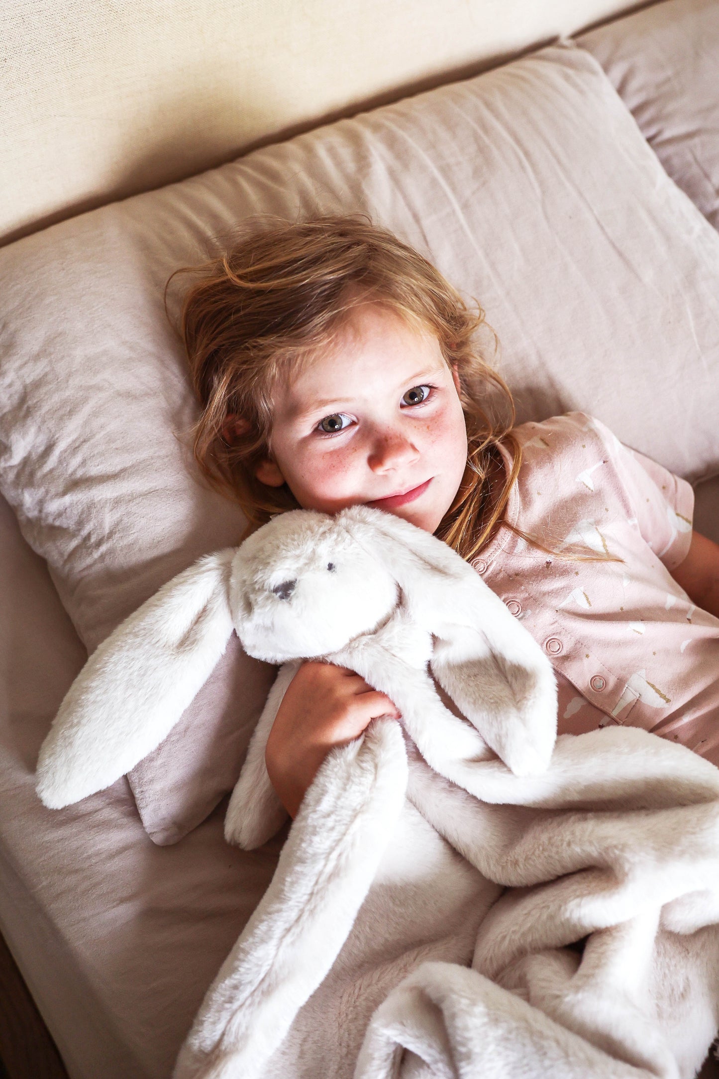 Soft ivory plush blanket with attached rabbit head and floppy ears, cuddled by child.