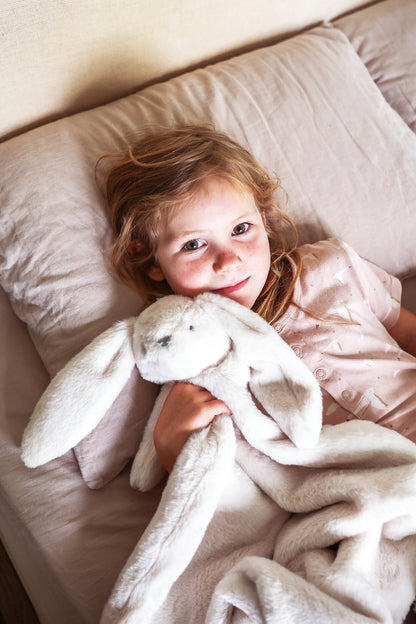 Soft ivory plush blanket with attached rabbit head and floppy ears, cuddled by child.