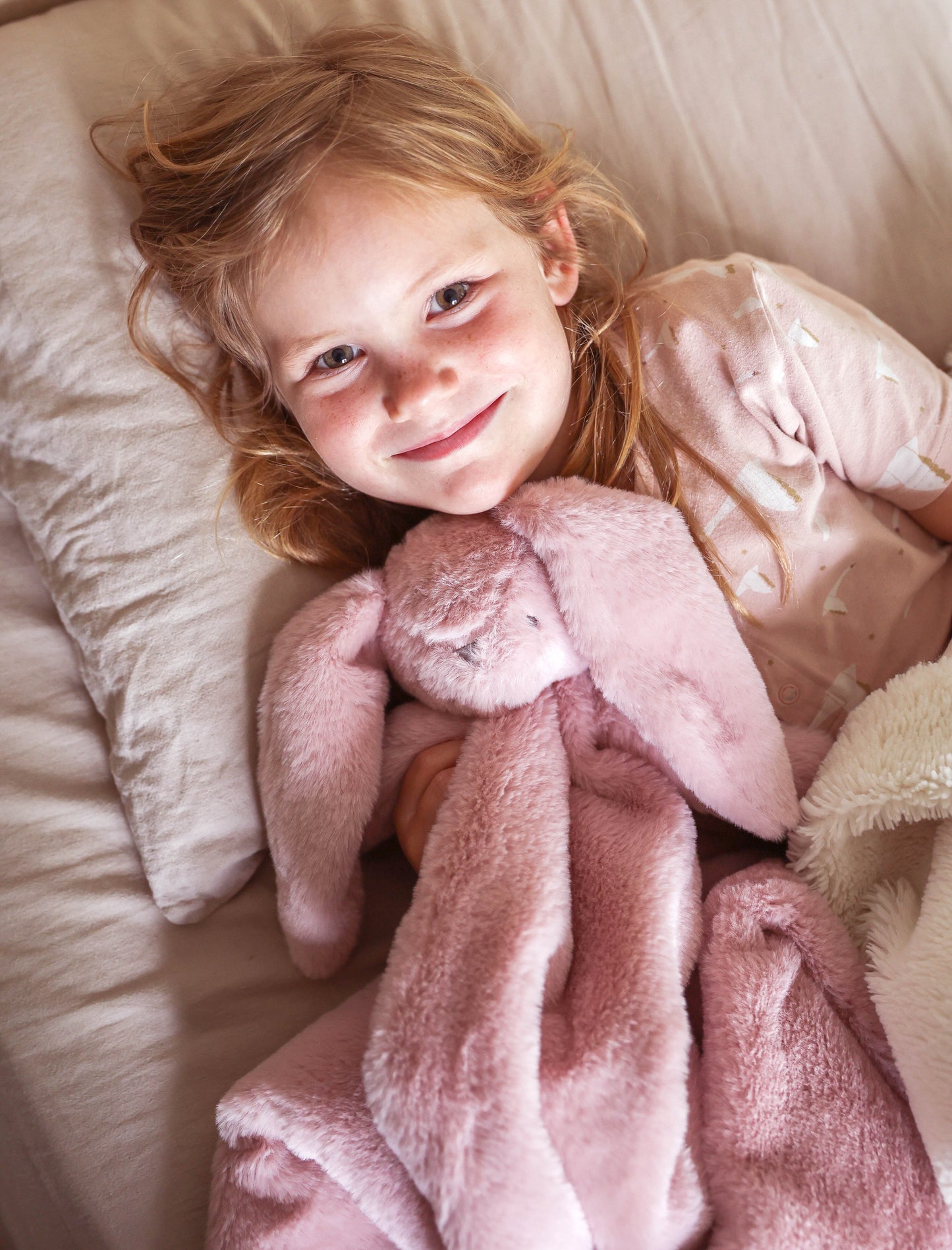 Soft pink plush bunny lovey blanket with floppy ears and a smooth texture held by a smiling child.