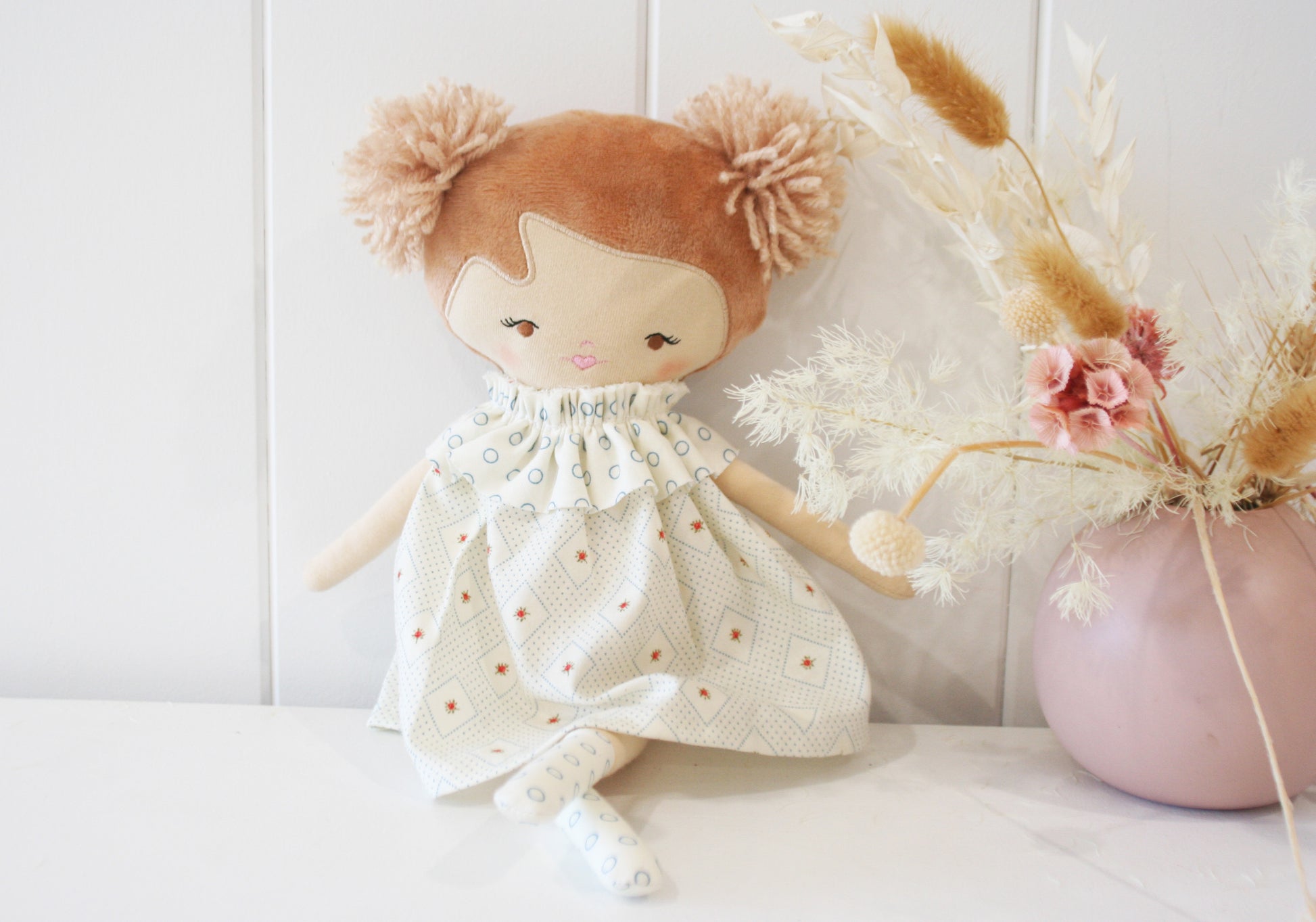 35cm soft cloth doll with brown yarn hair in pigtails wearing cream dress with blue and orange floral print.