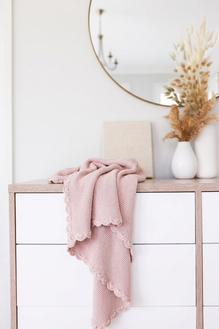 Petal pink knit mini blanket with moss stitch texture and scalloped edges draped over white dresser.