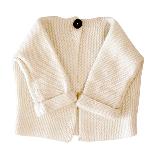 Cream-colored knitted baby jacket with long sleeves and a single large black button closure.