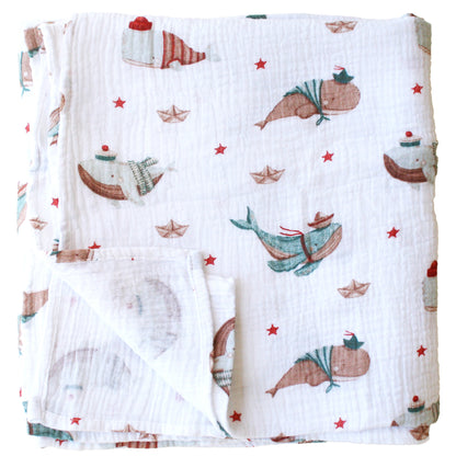 White muslin swaddle blanket with playful whales and red starfish pattern.