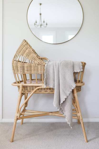 Soft latte-colored knit baby blanket with moss stitch draped over woven rattan bassinet.