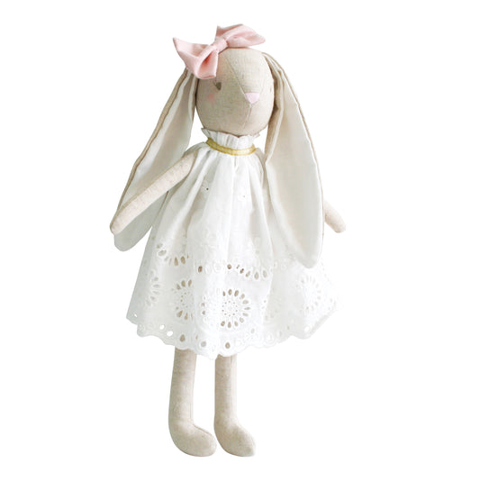 Soft beige bunny doll wearing a white eyelet broderie dress with a pink bow on its head.