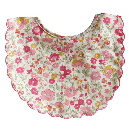 Round baby bib with scalloped edges, featuring pink, red, and yellow floral pattern on white fabric.