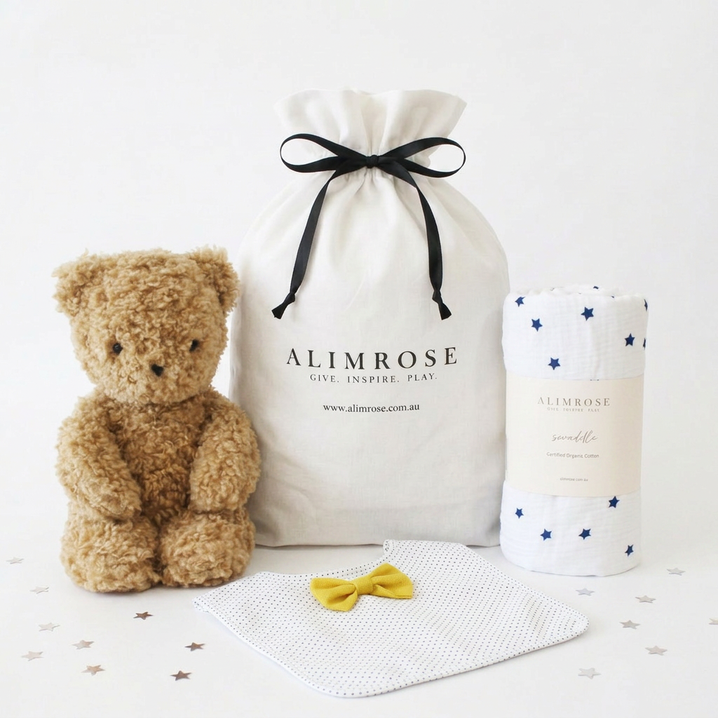 Navy star-patterned baby blanket, soft brown teddy bear, white bandana bib with yellow bow, and cream drawstring gift bag.