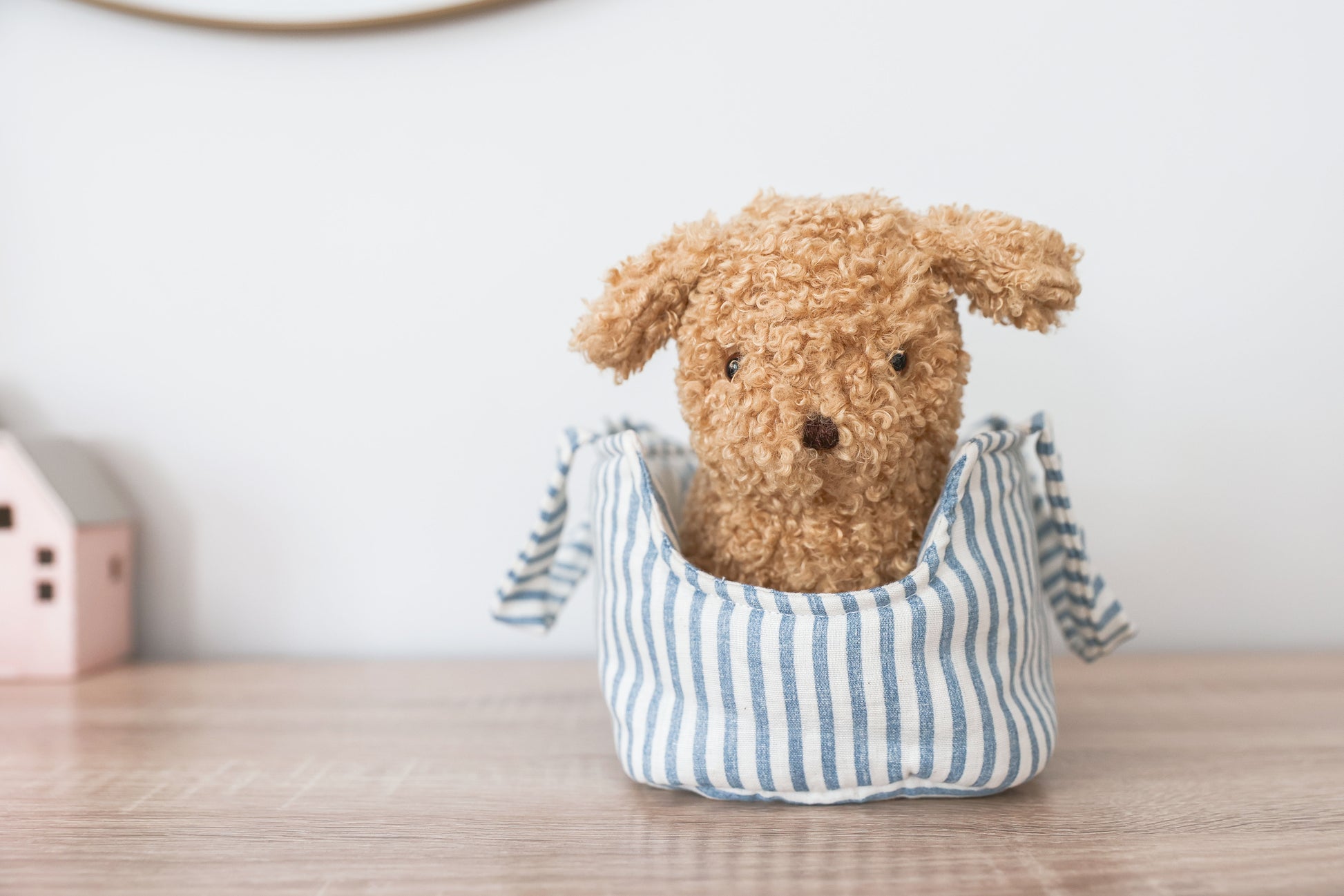 Soft tan plush puppy with curly fur sitting in a blue and white striped fabric carrier bag.