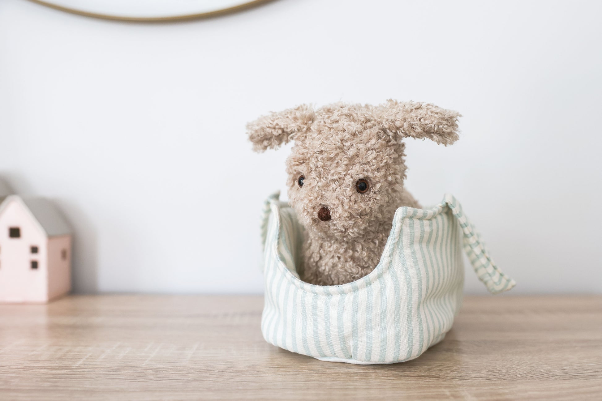 Soft beige plush puppy with floppy ears sitting in light blue and white striped fabric carrier bag on wooden surface.
