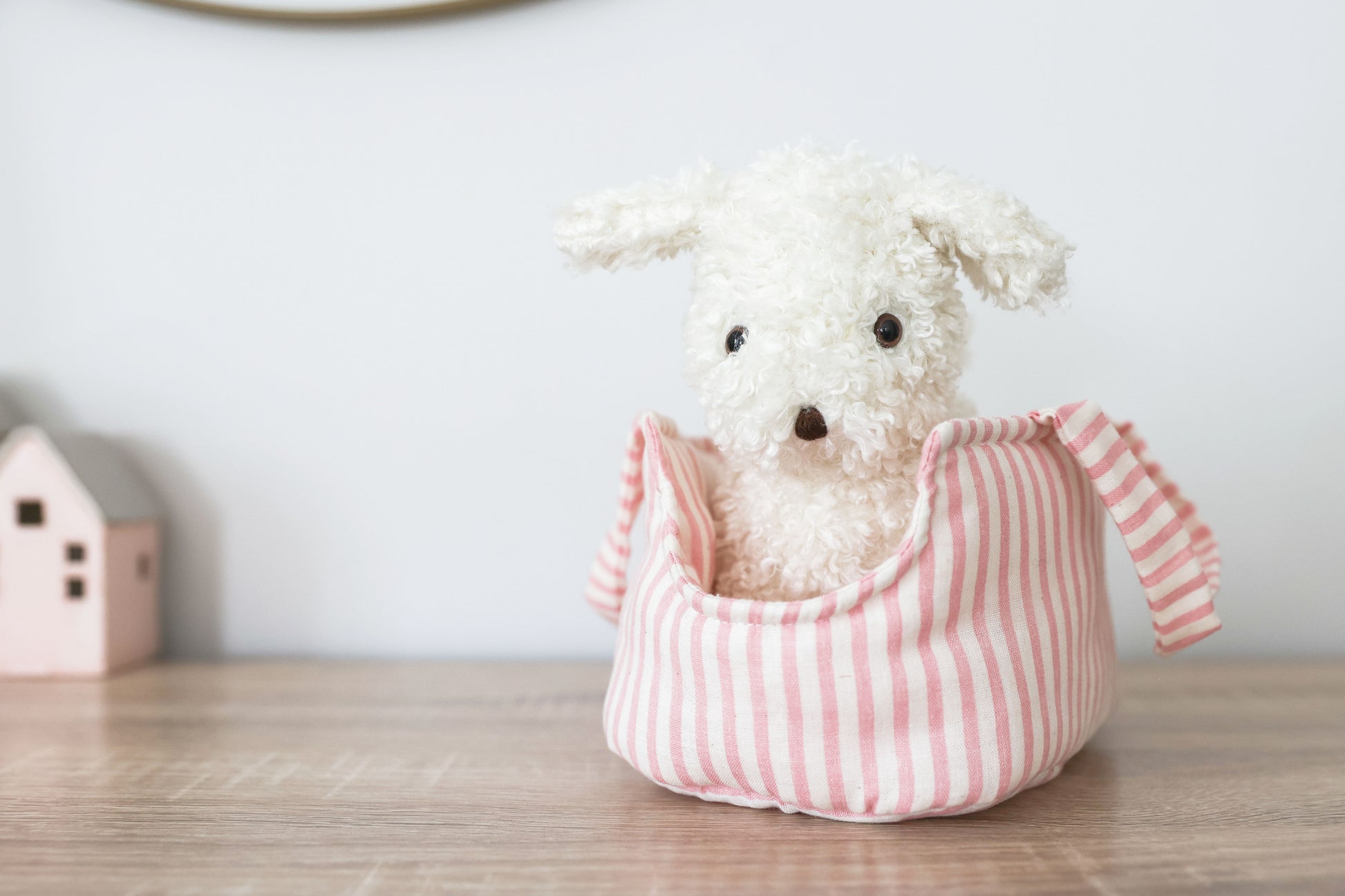 White fluffy plush puppy with black eyes and nose sitting inside a soft pink-and-white striped fabric carrier.