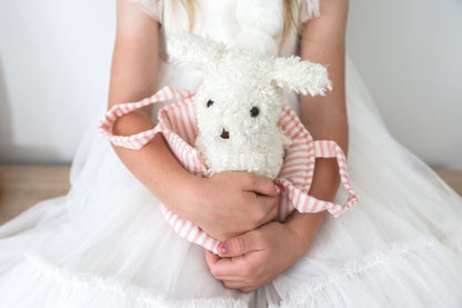 White fluffy plush puppy with black eyes and nose inside a pink and white striped fabric carrier, held by a child in a white