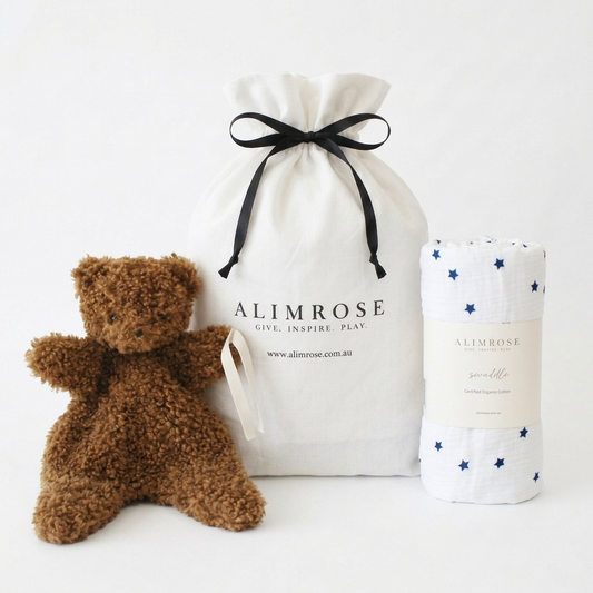 Brown curly plush teddy bear, white drawstring cotton bag with black ribbon, and white swaddle with navy blue stars pattern.