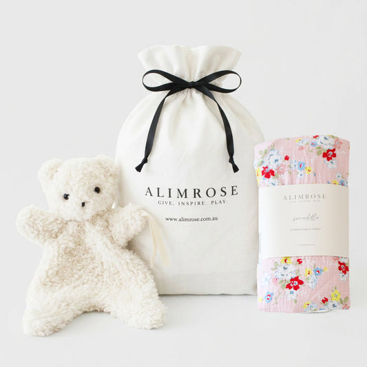 Pink floral print blanket, soft white teddy bear plush, and white drawstring pouch with black ribbon.