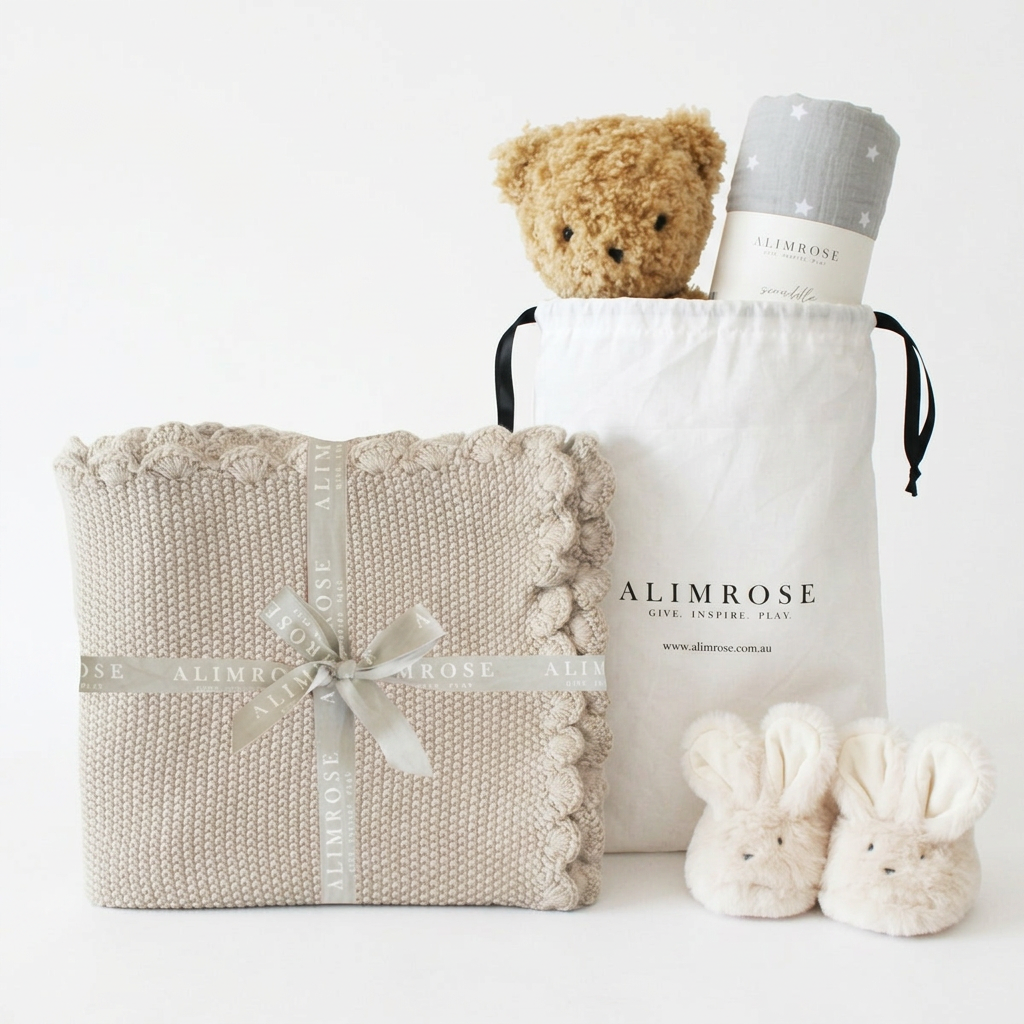 Neutral beige knit baby blanket with scalloped edges, tied with a cream ribbon, next to a white drawstring bag containing a.