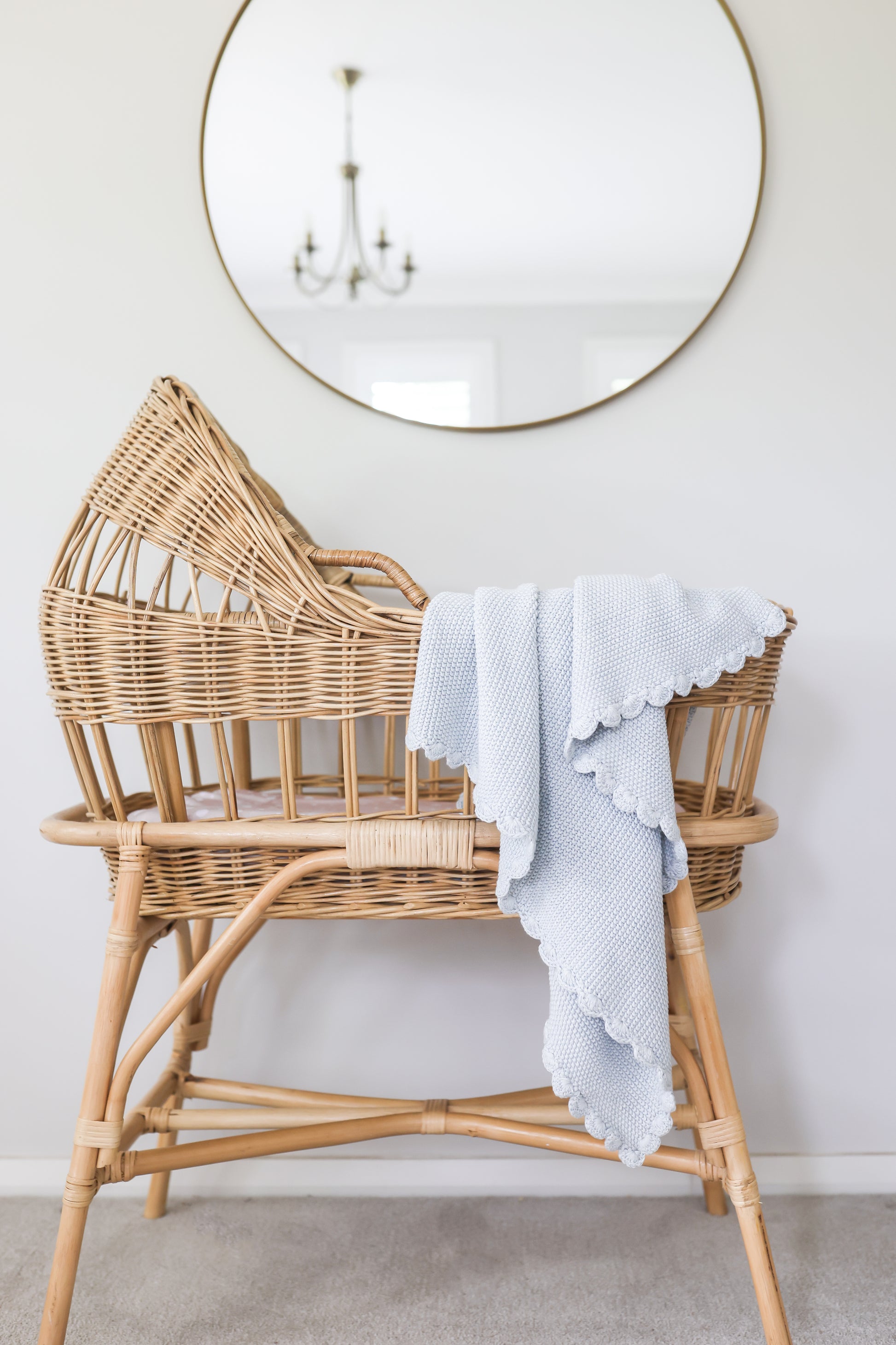 Powder blue knit baby blanket with moss stitch draped over natural rattan cradle with scalloped edges.
