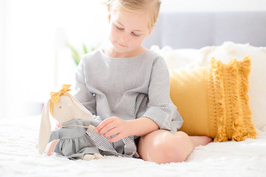 Young child playing with Alimrose Mini Sofia Bunny, a 27cm grey stuffed bunny in a stylish outfit.